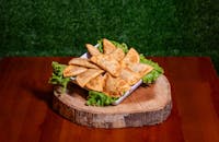 A plate of golden crispy samosas on lettuce, placed on a rustic wooden platter.